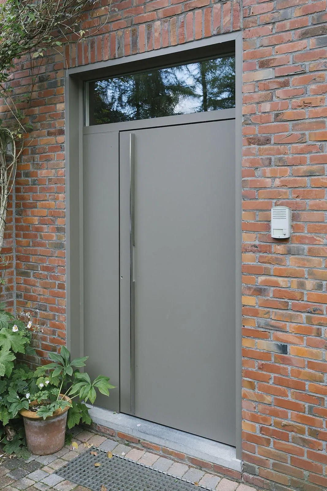 Graue maßgefertigte Aluminium-Haustür mit Oberlicht in einer Ziegelfassade